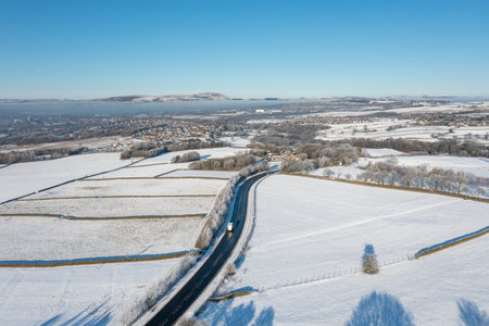 Aerial drone photo of the town of Mereclough in the town of Burnley in Lancashire, England showing the farmers fields on a snowy winters day in the UK with snow covering the fields and a blue sky.の写真素材