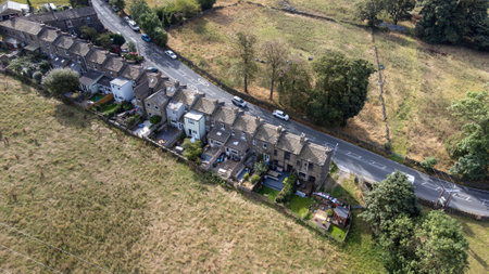 Aerial drone photo of the beautiful village of East Morton in Keighley in Yorkshire in the UK, showing old historic rows of traditional terraced houses by a road surrounded by farmers fields.の写真素材