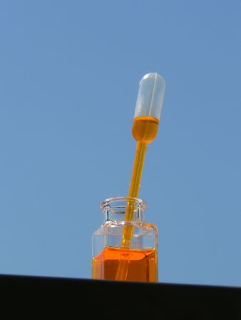pipet in orange container filled with orange reagent over blue skyの写真素材