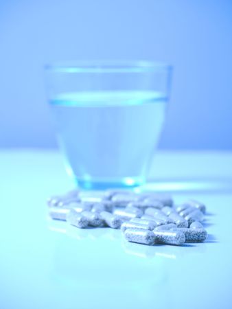 Blue tinted picture of  pills on reflective surface with glass of water with selective focus on pillsの写真素材