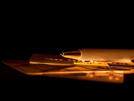Golden credit cards cut with pen on black reflective surface の写真素材