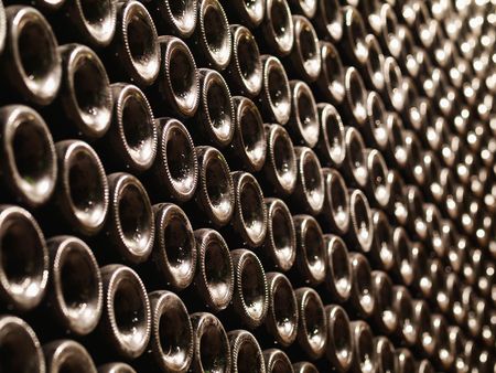 Row of Bordeaux wine bottles stacked in a cellar with shallow depth of field