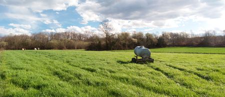 Panoramic view of  a metallic waterer in the middle of a fresh green field of grass