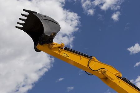 Yellow excavator scoop in cloudy sky.