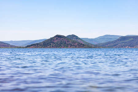A high angle shot of a lake surrounded by hills under a blue skyの写真素材