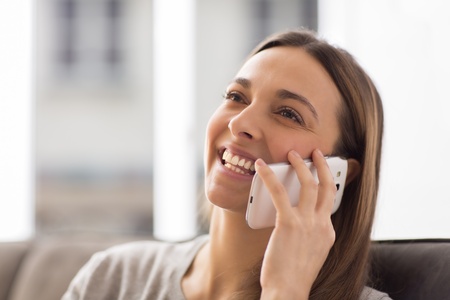 Pretty young female using white mobile phone at home smilingの写真素材