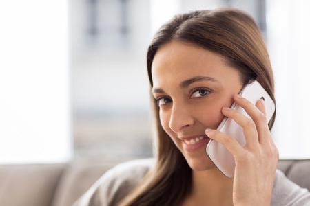 Pretty young female using white mobile phone at home looking at the cameraの写真素材