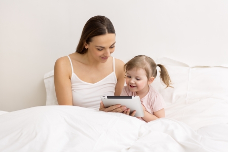 little girl surfing on internet wiht her mom in the white bedroomの写真素材