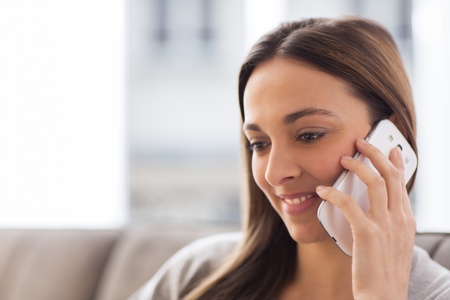 Pretty young woman using white mobile phone at homeの写真素材