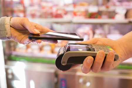 Woman paying with NFC technology on mobile phone, in supermarket butcherの写真素材