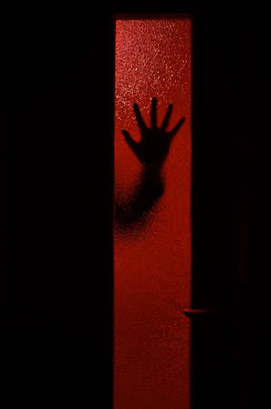 Mysterious arm on the reddish glass behind the doorの写真素材