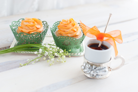 Cupcakes with orange cream with coffee cup and flowersの写真素材