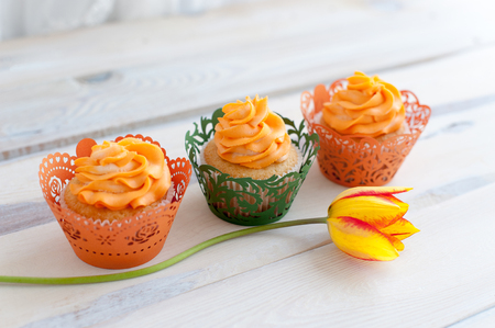 Three delicious cupcakes with orange cream and orange tulipsの写真素材
