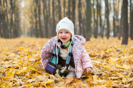 Baby sitting in autumn forest and cryingの写真素材