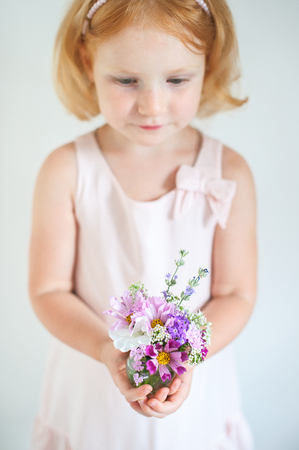 Beautiful red-haired child holding a bouquet of summer flowersの写真素材