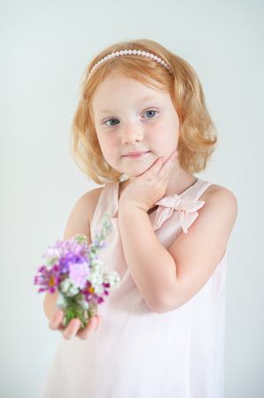 Beautiful red-haired child holding a bouquet of summer flowersの写真素材