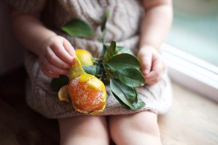 Girl sits on a window with a tangerineの写真素材