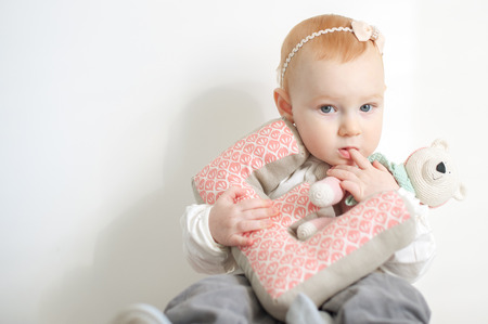 Little red-haired girl with toys in her hands sucks her fingerの写真素材