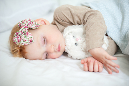 Red-haired girl is sleeping with a soft toyの写真素材