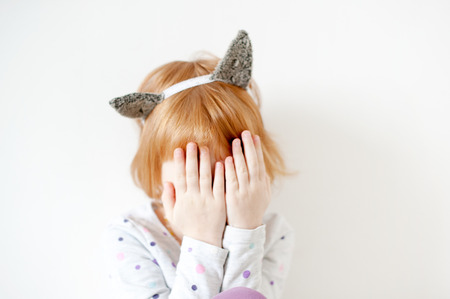 Red-haired girl with cat's ears on her head covers her face with handsの写真素材