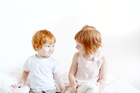 Red-haired brother and sister are sitting on the bedの写真素材