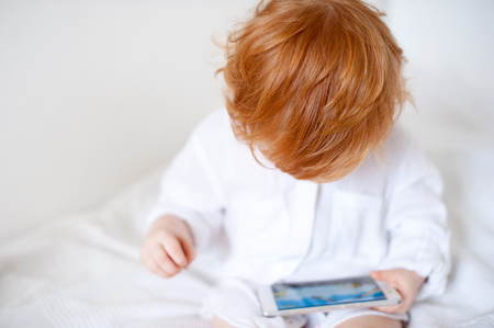 Red-haired boy looking into the phone and playing the gameの写真素材