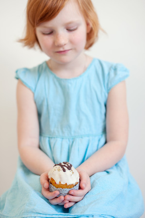 Red-haired girl in a blue dress is holding an Easter cakeの写真素材