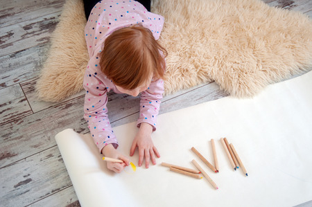Girl draws with colored pencils, lying on the floorの写真素材