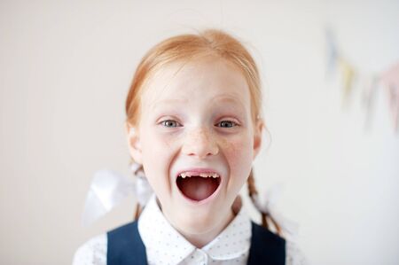 Smiling red-haired schoolgirl without teeth indoorsの写真素材
