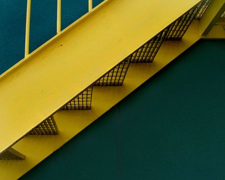 A detail image of a yellow grated stairway infront of a green buildingの写真素材