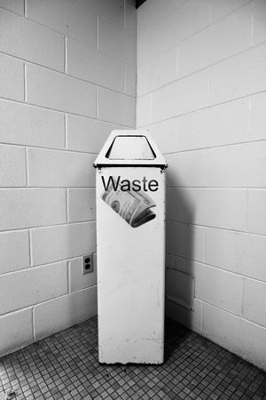 Retro black and white image of an old garbage can showing an american $20 bill roll and the word wasteの写真素材