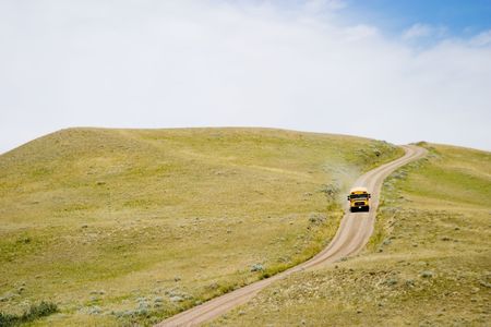 A yellow school bus going down a small dirt roadの写真素材