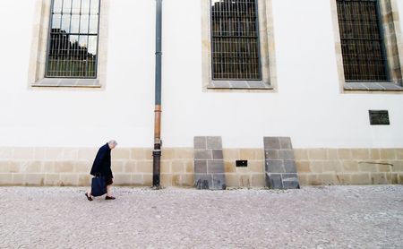 An abstract image of an old woman hunched over walking by a large church (Betlemske Nam) with tall gothic windows in Prague, Czech Republic.の写真素材