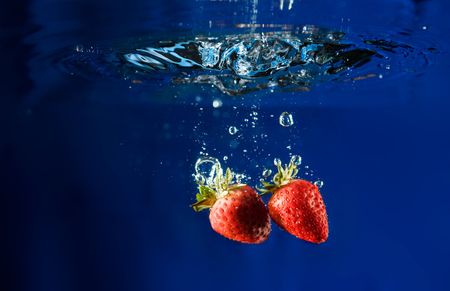 Two strawberries splashing in waterの写真素材