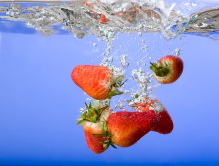 Strawberries falling in blue water with splash and bubblesの写真素材