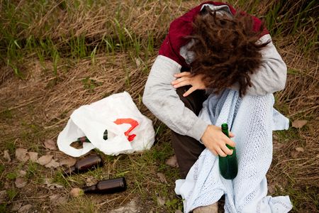 A drunk person sitting in a ditch with a wine bottleの写真素材
