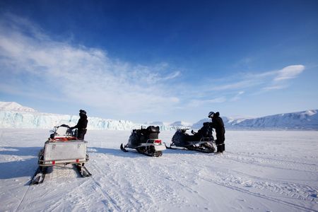 Three snowmobiles in front of a glacier, Svalbard, Norwayの写真素材