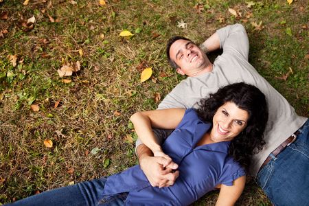 A happy couple daydreaming in a park on grass - sharp focus on womanの写真素材