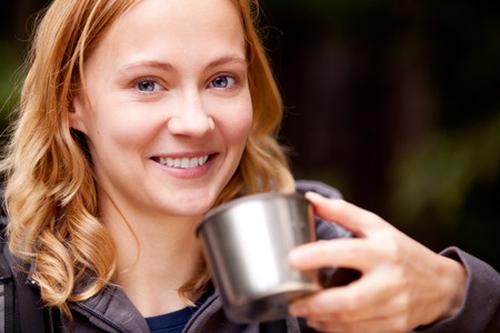 A young beautiful woman outdoors on a campnig trip taking a drinkの写真素材