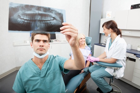 Radiodentist checking x-ray with assistant and patient having conversation in the backgroundの写真素材