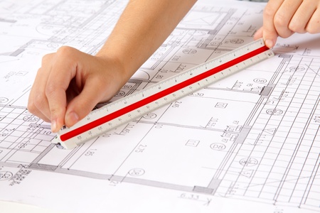Two hands using a scale ruler on a set of blueprintsの写真素材