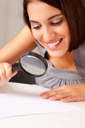 A prety brunette woman looking at a paper with a magnifying glassの写真素材