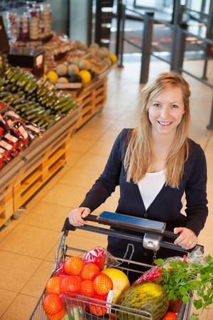 Smiling woman looking at camera while holding shopping cart in storeの写真素材