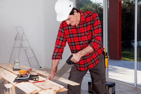 A construction worker using a hand wood saw while wearing a white safety helmetの写真素材