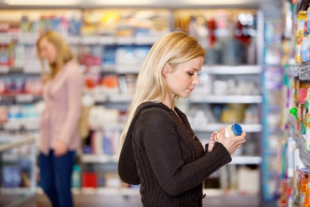Young woman comparing products in the supermarket with people in the backgroundの写真素材