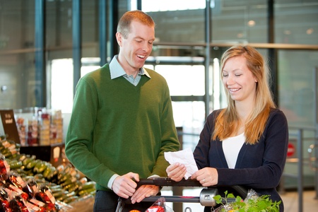 A happy couple with a shopping cart and grocery list in a supermarketの写真素材