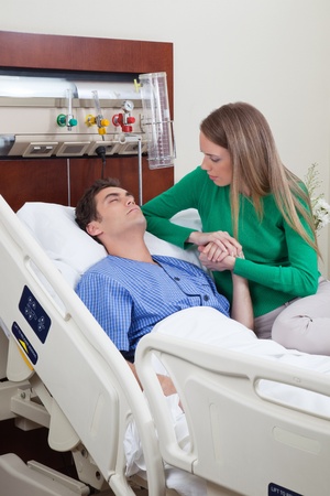Man on a hospital bed with woman holding his hand with concernの写真素材