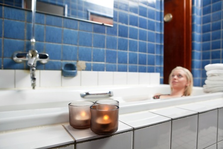 Beautiful young woman relaxing in bathtub with candles in foregroundの写真素材
