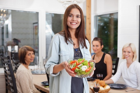 Portrait of happy female holding bowl of vegetables while her friends sitting in backgroundの写真素材