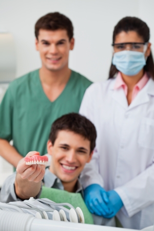Male patient showing dental molds with dentist standing in background with her colleagueの写真素材